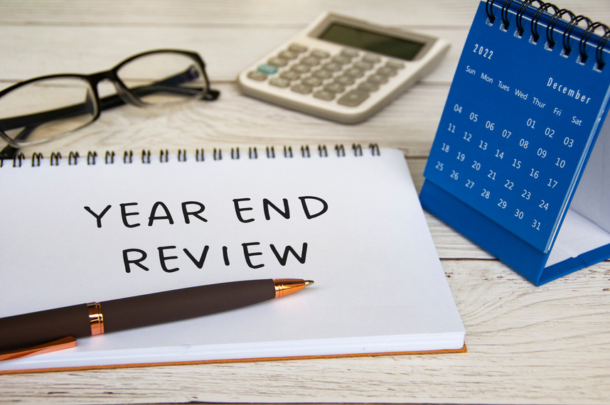 Year end review text on notepad with December calendar, glasses, calculator and pen. Year end review concept.